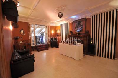 Jardin avec pelouse, tables et chaises rouges, scène en bois, entouré d'arbres et d'une maison à colombages.