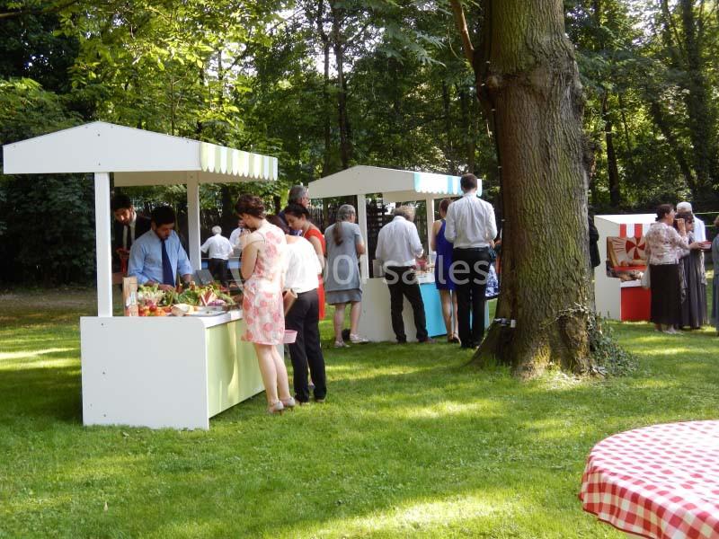 Des stands de nourriture en plein air dans un parc, avec des personnes choisissant des plats sous un ciel ensoleillé.