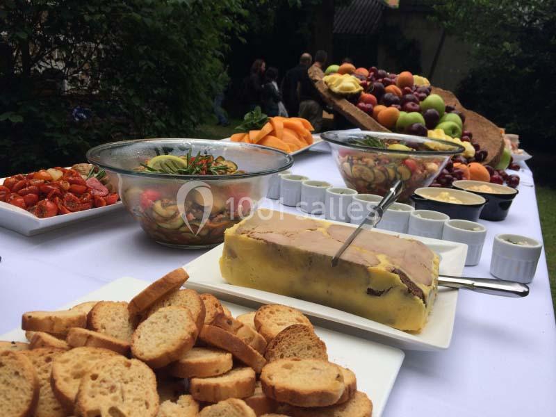 Buffet en extérieur avec terrine, croûtons, salades, fruits frais et sauces disposés sur une table blanche.