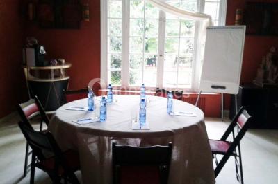 Jardin avec pelouse, tables et chaises rouges, scène en bois, entouré d'arbres et d'une maison à colombages.