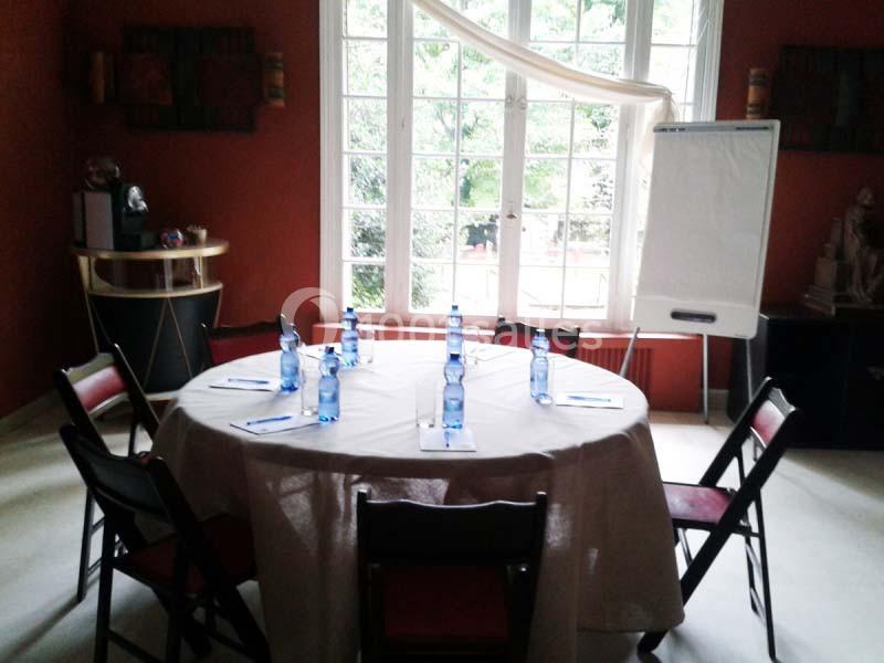 Table ronde dressée avec des bouteilles d'eau et des blocs-notes, entourée de chaises, devant une baie vitrée.