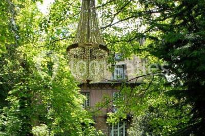 Jardin avec pelouse, tables et chaises rouges, scène en bois, entouré d'arbres et d'une maison à colombages.