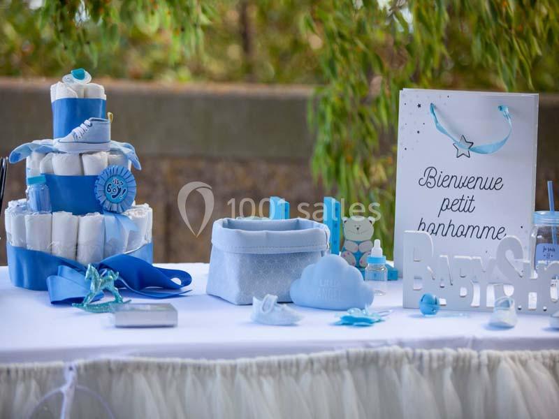 Table décorée pour une fête de naissance avec gâteau de couches, accessoires bleus et panneau ’Bienvenue petit bonhomme’.