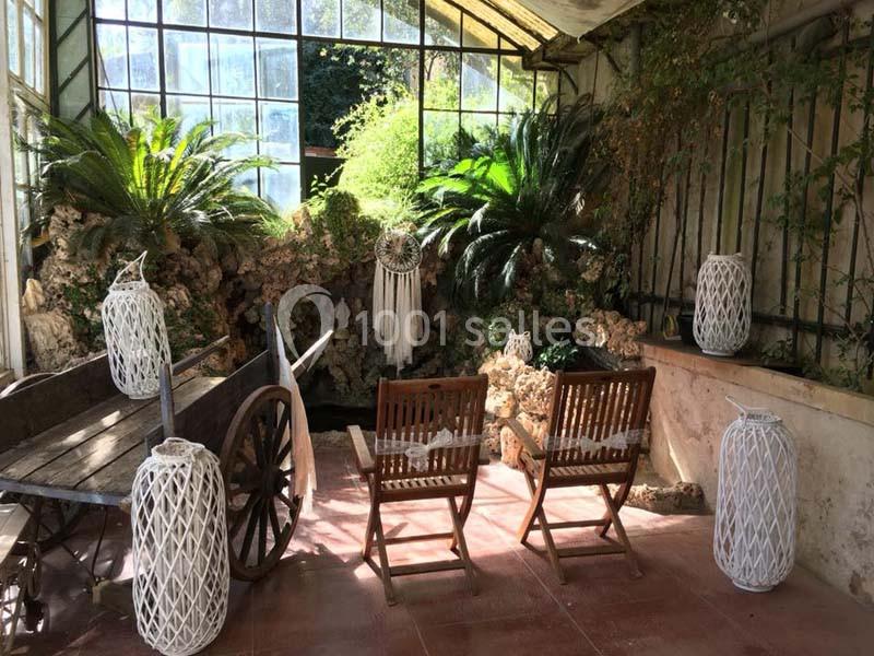 Deux chaises en bois face à un décor végétal luxuriant dans une véranda lumineuse avec des lanternes décoratives.