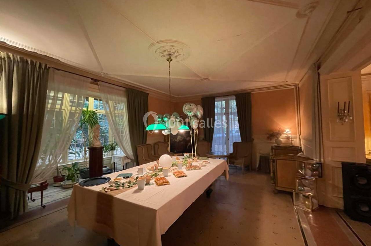Salle élégante avec une grande table dressée pour un buffet, éclairée par des lampes suspendues et entourée de rideaux.