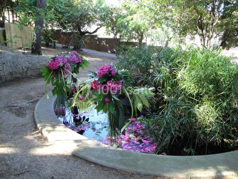 Bassin circulaire entouré de végétation, décoré de fleurs roses flottantes et suspendues.