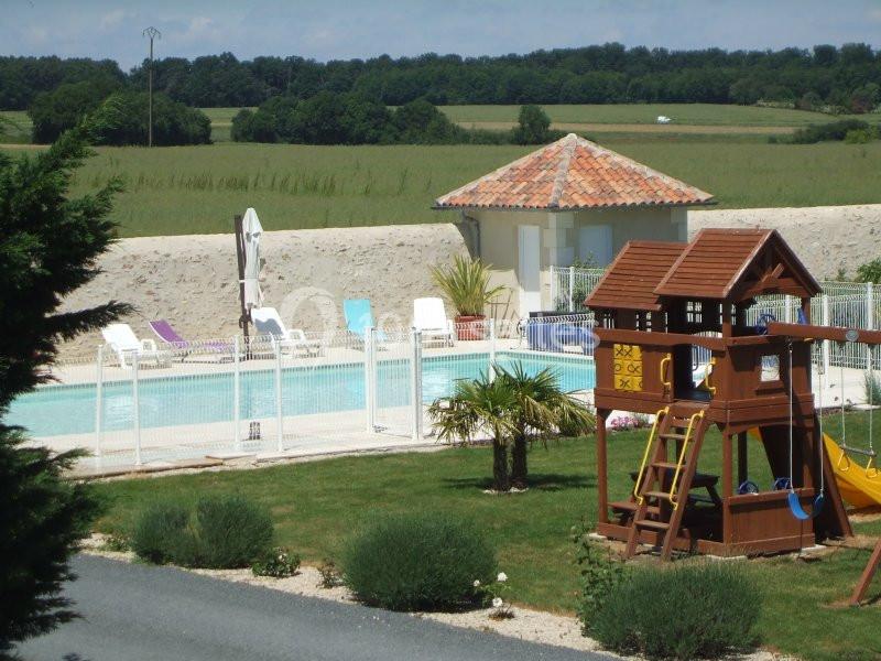 Piscine extérieure clôturée avec transats, cabanon et aire de jeux pour enfants dans un cadre verdoyant.