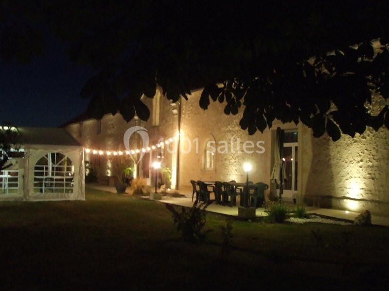 Façade d'un bâtiment en pierre éclairé la nuit, avec guirlandes lumineuses et une tente blanche à gauche.