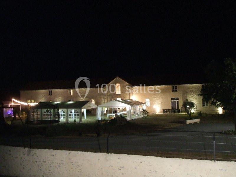 Bâtiment en pierre éclairé la nuit, avec des tentes blanches installées dans une cour devant.