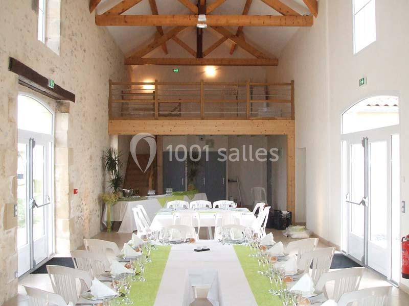 Salle lumineuse avec poutres apparentes, tables dressées avec nappes blanches et chemins de table verts.