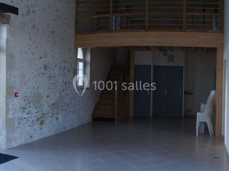 Intérieur d'une pièce avec un mur en pierre, un escalier en bois, des portes grises et des chaises empilées.