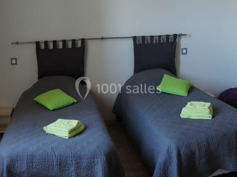 Deux lits simples avec couvre-lits gris, oreillers verts et serviettes pliées assorties posées dessus.