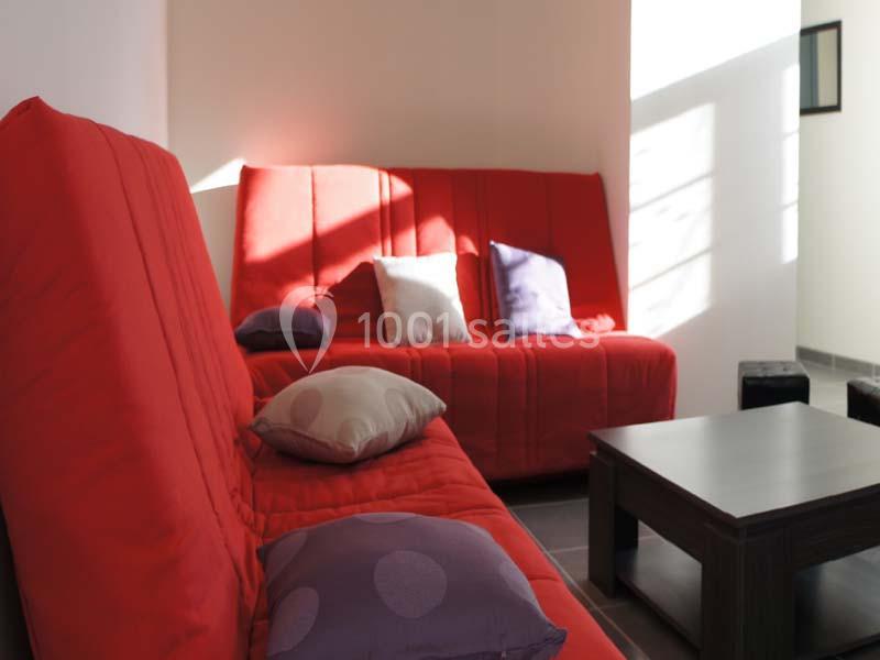 Deux canapés rouges avec des coussins colorés entourent une table basse dans une pièce lumineuse.