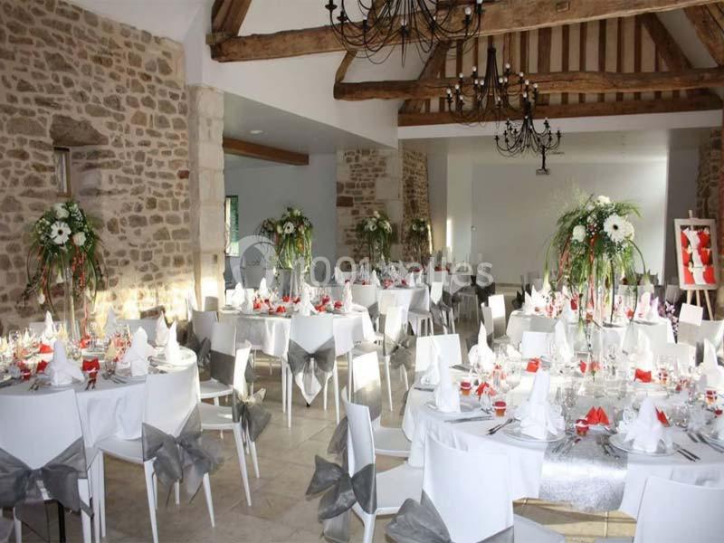 Salle de réception décorée avec des tables rondes, nappes blanches, chaises ornées de nœuds gris et arrangements floraux.