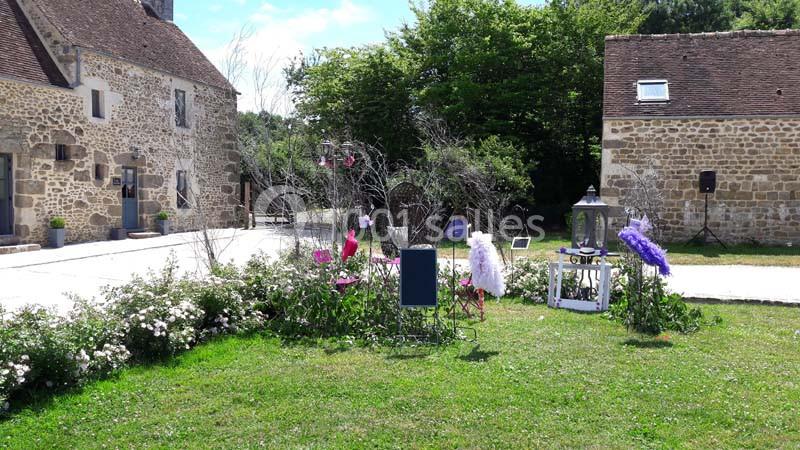 Jardin fleuri avec décorations et lanternes, entouré de bâtiments en pierre sous un ciel dégagé.