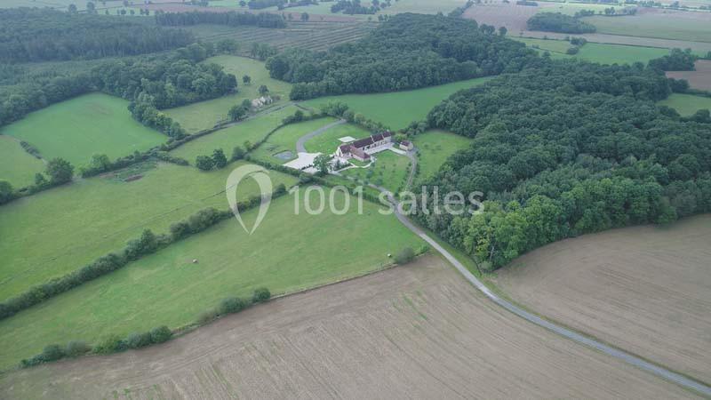 Vue aérienne d'une propriété entourée de champs, de prairies et de forêts dans un paysage rural.
