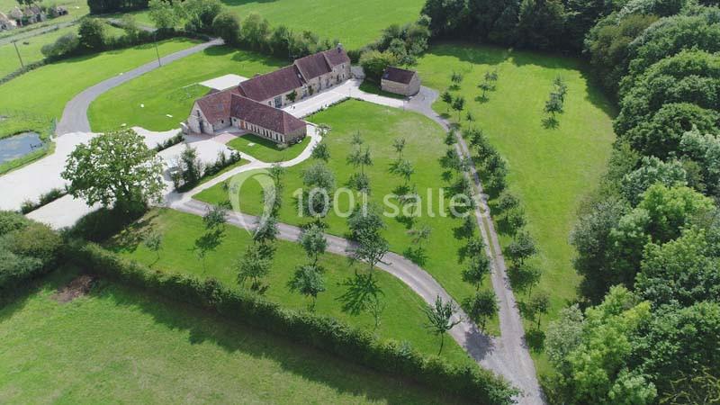 Vue aérienne d'une grande maison entourée d'un jardin arboré, d'une allée sinueuse et de prairies verdoyantes.