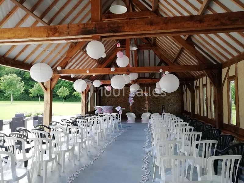 Salle de réception décorée avec des lanternes suspendues, des rangées de chaises blanches et noires, et vue sur l'extérieur…