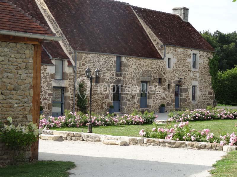 Maison en pierre avec toit en tuiles, entourée d'un jardin fleuri et d'une allée en gravier.