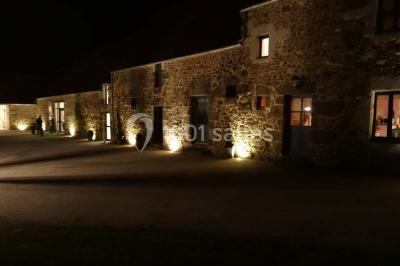 Chambre mansardée avec quatre lits simples, couvertures bleues et étagère en bois clair contre un mur gris.