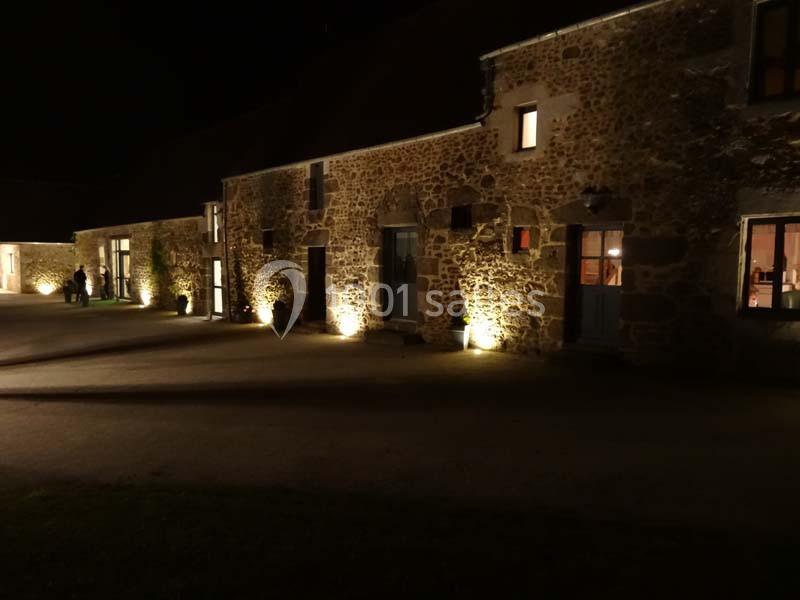 Façade en pierre d'un bâtiment éclairé par des lumières au sol, de nuit, avec des fenêtres illuminées.