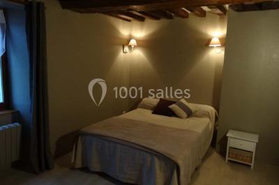 Chambre mansardée avec quatre lits simples, couvertures bleues et étagère en bois clair contre un mur gris.