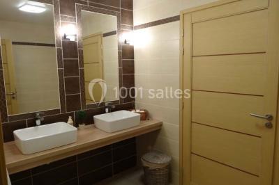 Chambre mansardée avec quatre lits simples, couvertures bleues et étagère en bois clair contre un mur gris.