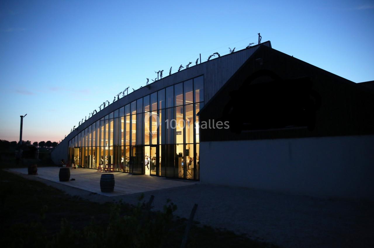 Bâtiment moderne avec de grandes baies vitrées illuminées, photographié au crépuscule.