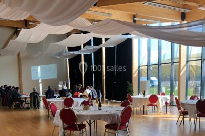 Salle lumineuse accueillant un salon avec des stands, des visiteurs et des tables exposant divers produits et services.