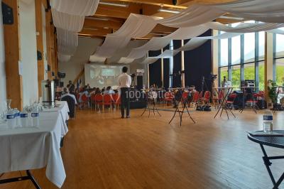 Salle lumineuse accueillant un salon avec des stands, des visiteurs et des tables exposant divers produits et services.