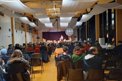Salle lumineuse accueillant un salon avec des stands, des visiteurs et des tables exposant divers produits et services.