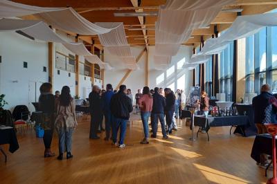 Salle lumineuse accueillant un salon avec des stands, des visiteurs et des tables exposant divers produits et services.
