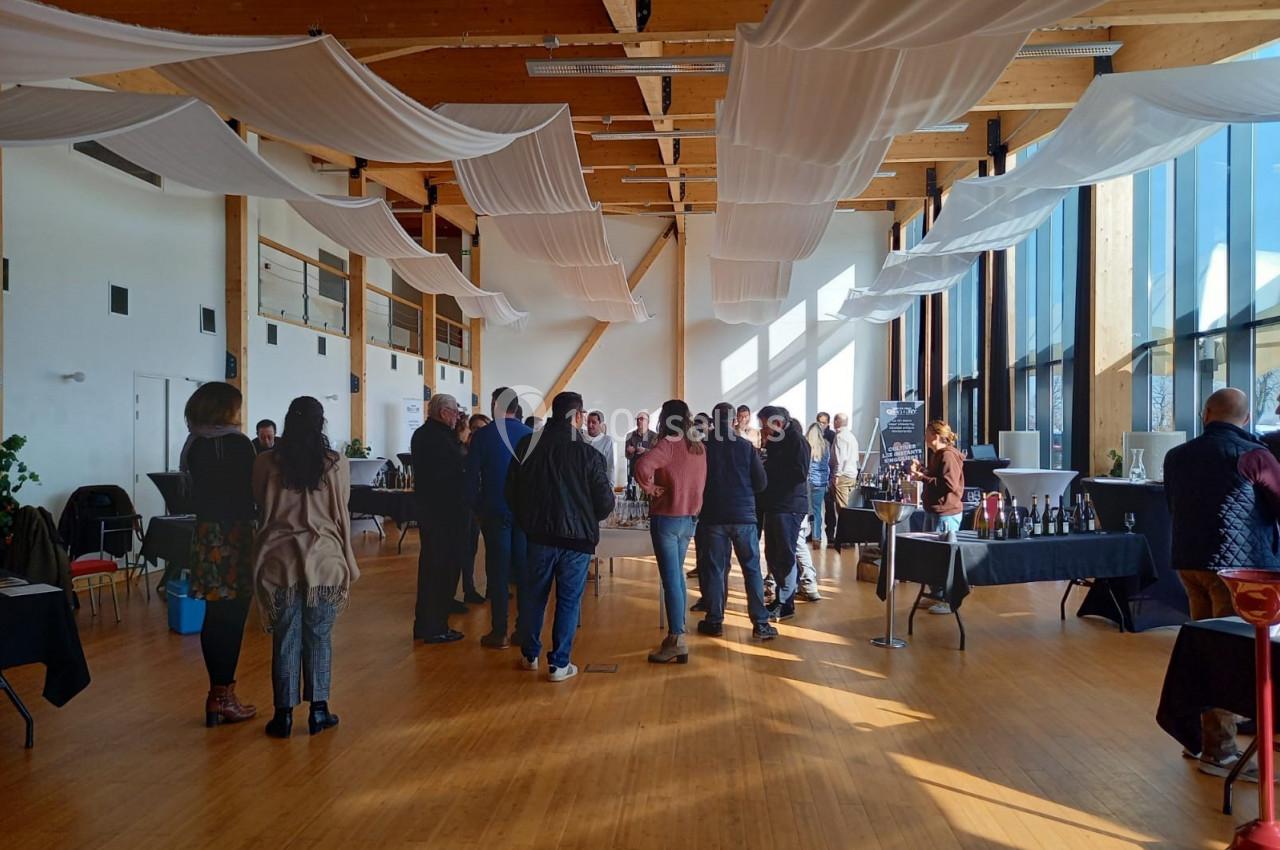 Des personnes discutent et dégustent dans une salle lumineuse avec des stands de présentation et un plafond décoré de…
