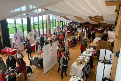 Salle lumineuse accueillant un salon avec des stands, des visiteurs et des tables exposant divers produits et services.