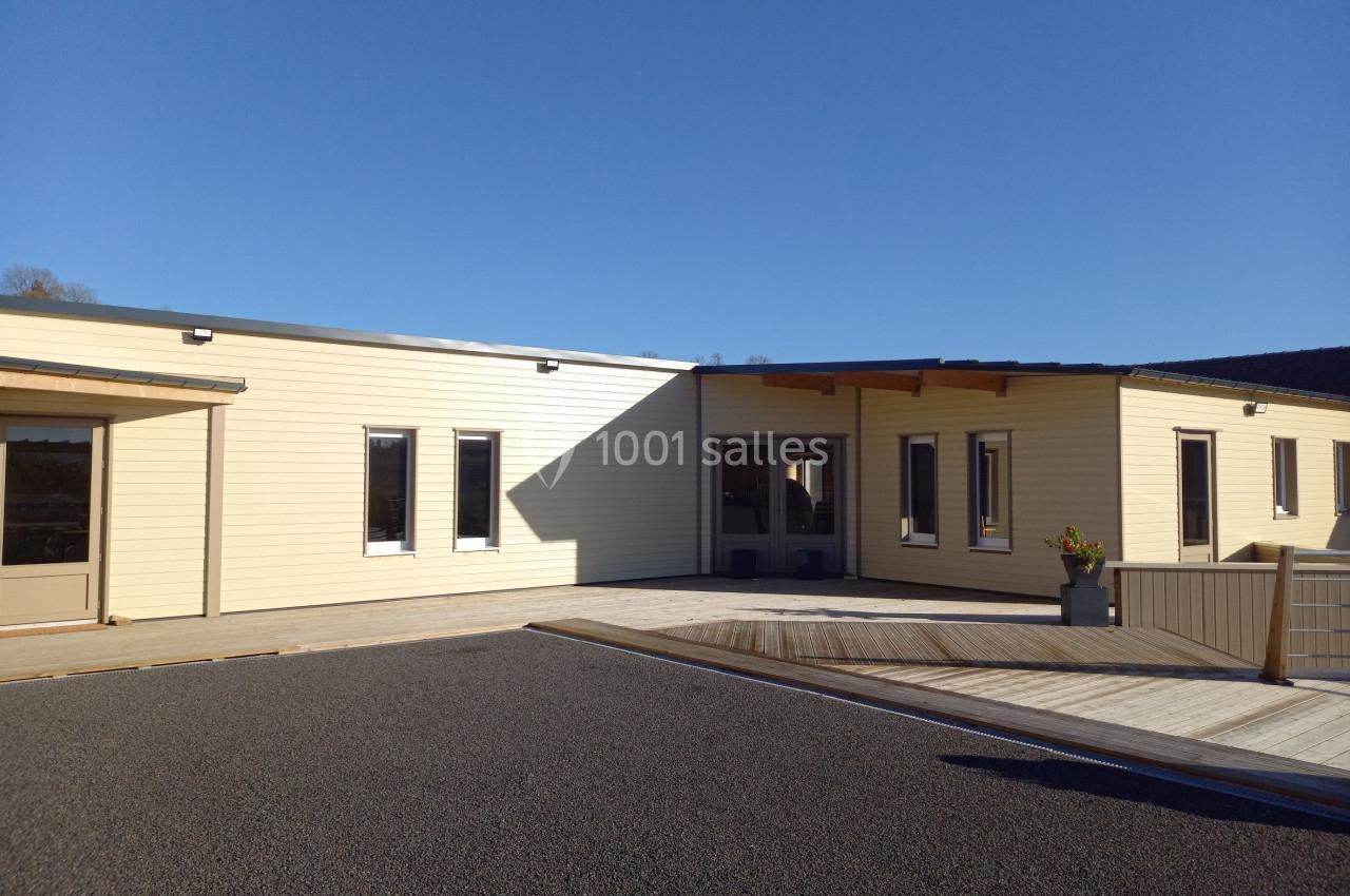 Bâtiment moderne en bois clair avec plusieurs fenêtres, une entrée principale et un espace extérieur ensoleillé.