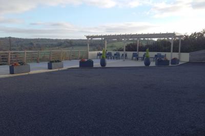 Chambre simple avec un lit double, une table en bois, une chaise et une lumière murale, donnant sur une porte vitrée.