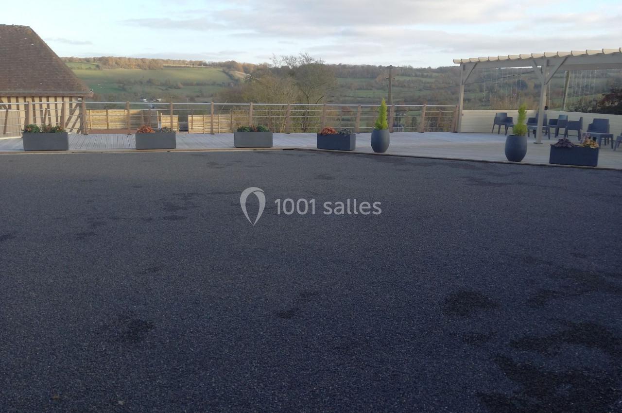 Cour extérieure avec sol en gravier, bordée de jardinières et offrant une vue sur un paysage vallonné sous un ciel…