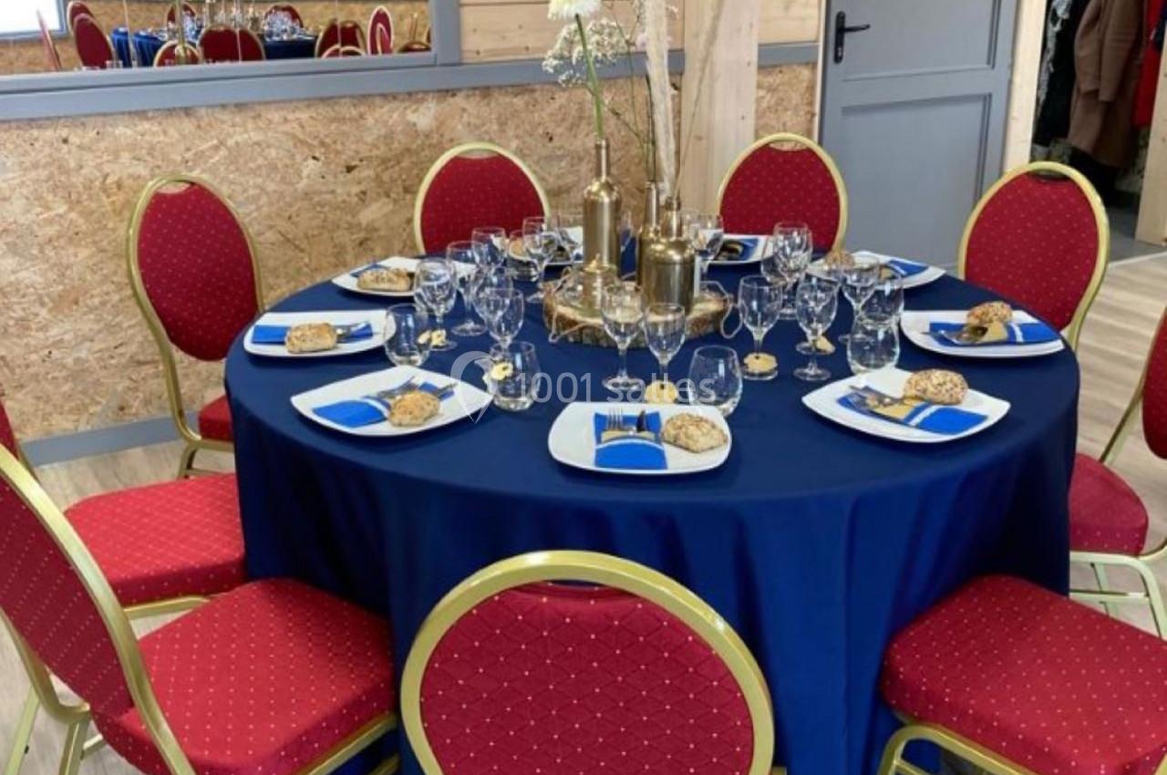 Table ronde dressée avec une nappe bleue, entourée de chaises rouges, décorée pour un repas avec vaisselle et ornements.