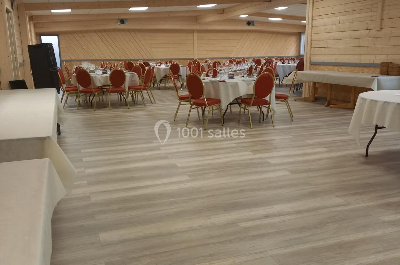 Salle de réception avec tables rondes dressées et chaises rouges, éclairée par un plafond à dalles blanches.