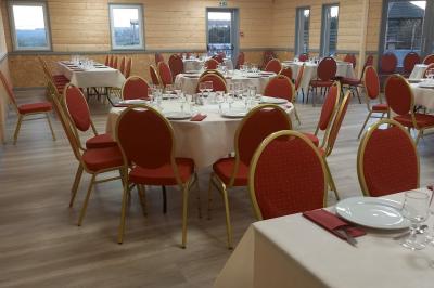 Chambre simple avec un lit double, une table en bois, une chaise et une lumière murale, donnant sur une porte vitrée.