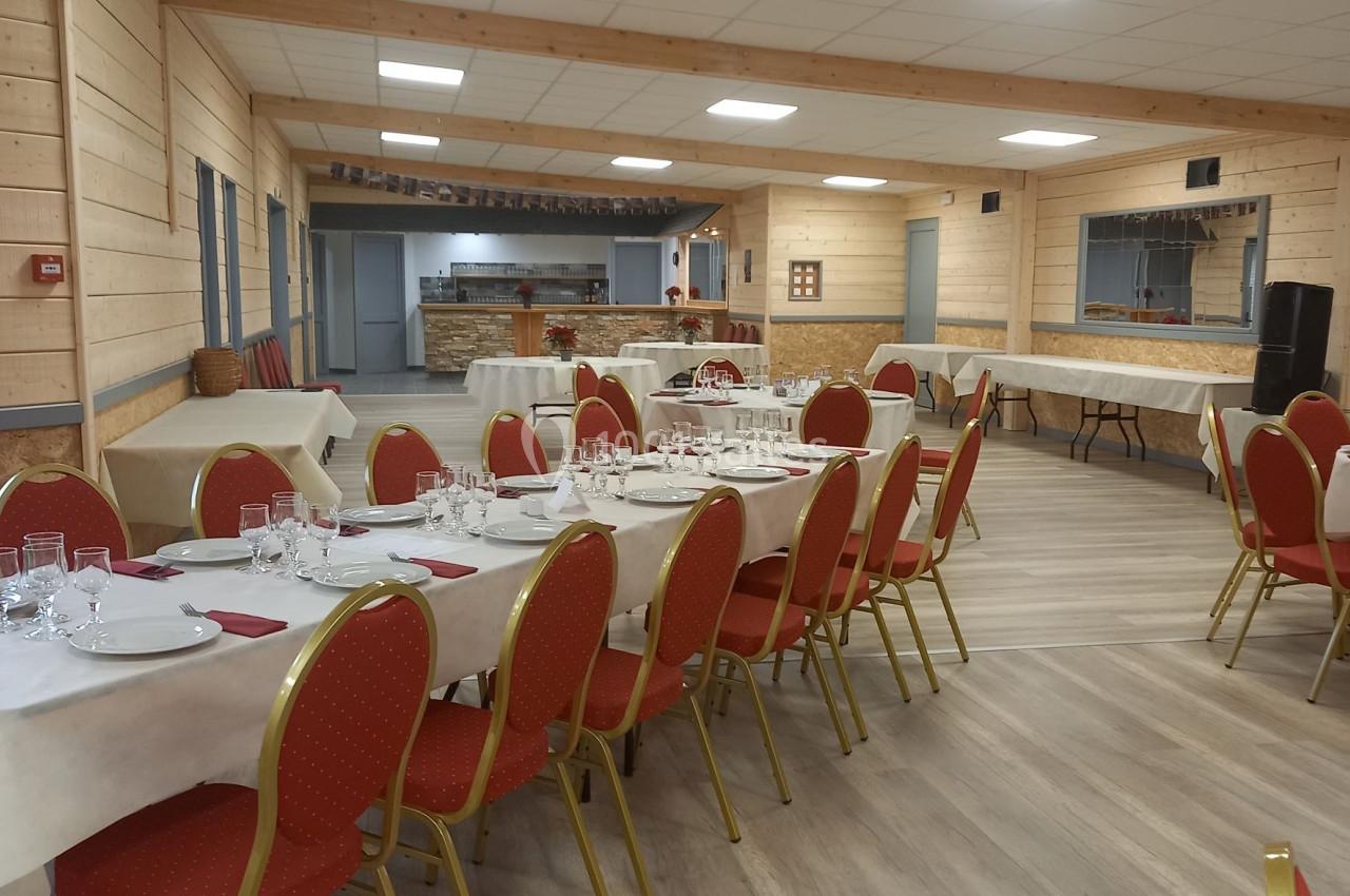 Salle lumineuse avec tables dressées, chaises rouges et parquet clair, prête pour un repas ou un événement.