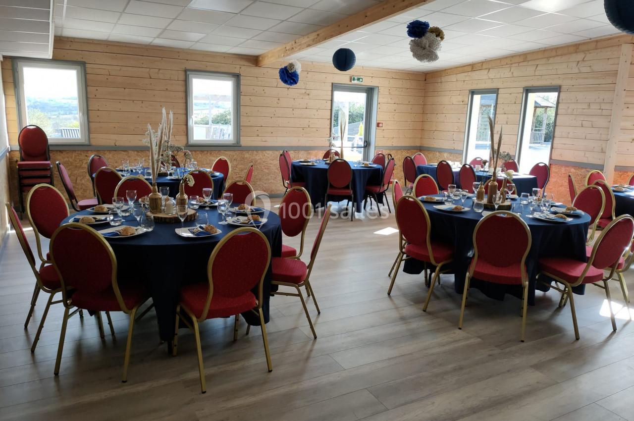 Salle décorée avec des tables rondes dressées, chaises rouges et fenêtres laissant entrer la lumière naturelle.