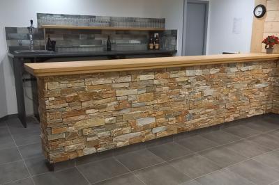 Chambre simple avec un lit double, une table en bois, une chaise et une lumière murale, donnant sur une porte vitrée.