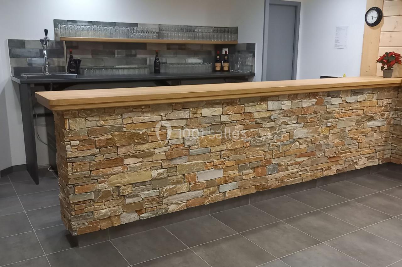 Comptoir en pierre avec plan de travail en bois, situé dans une pièce lumineuse avec carrelage gris au sol.