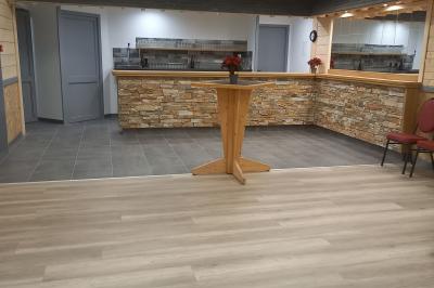 Chambre simple avec un lit double, une table en bois, une chaise et une lumière murale, donnant sur une porte vitrée.