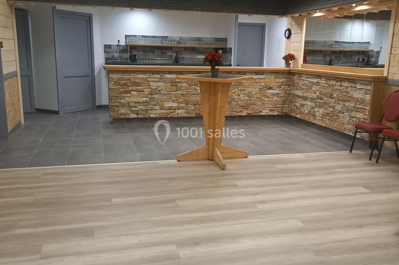 Salle avec un comptoir en pierre, tables hautes en bois, sol en parquet et carrelage, décorée de guirlandes.
