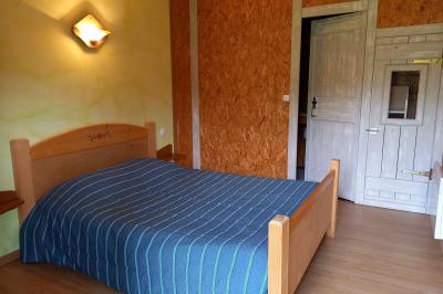 Chambre simple avec un lit double, une table en bois, une chaise et une lumière murale, donnant sur une porte vitrée.