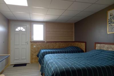 Chambre simple avec un lit double, une table en bois, une chaise et une lumière murale, donnant sur une porte vitrée.