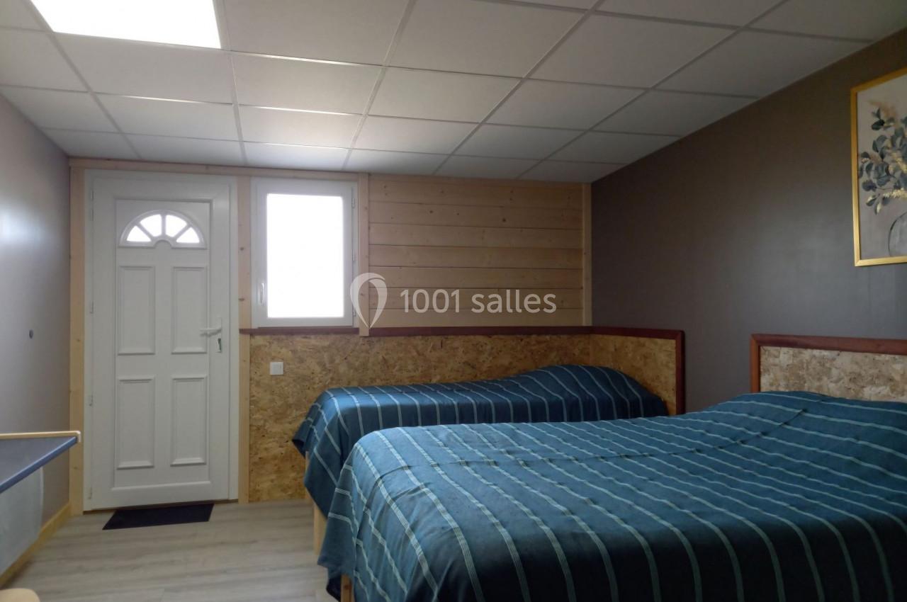 Deux lits simples avec couvre-lits rayés bleus dans une chambre sobre, éclairée par une fenêtre et une porte blanche.