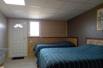 Chambre simple avec un lit double, une table en bois, une chaise et une lumière murale, donnant sur une porte vitrée.